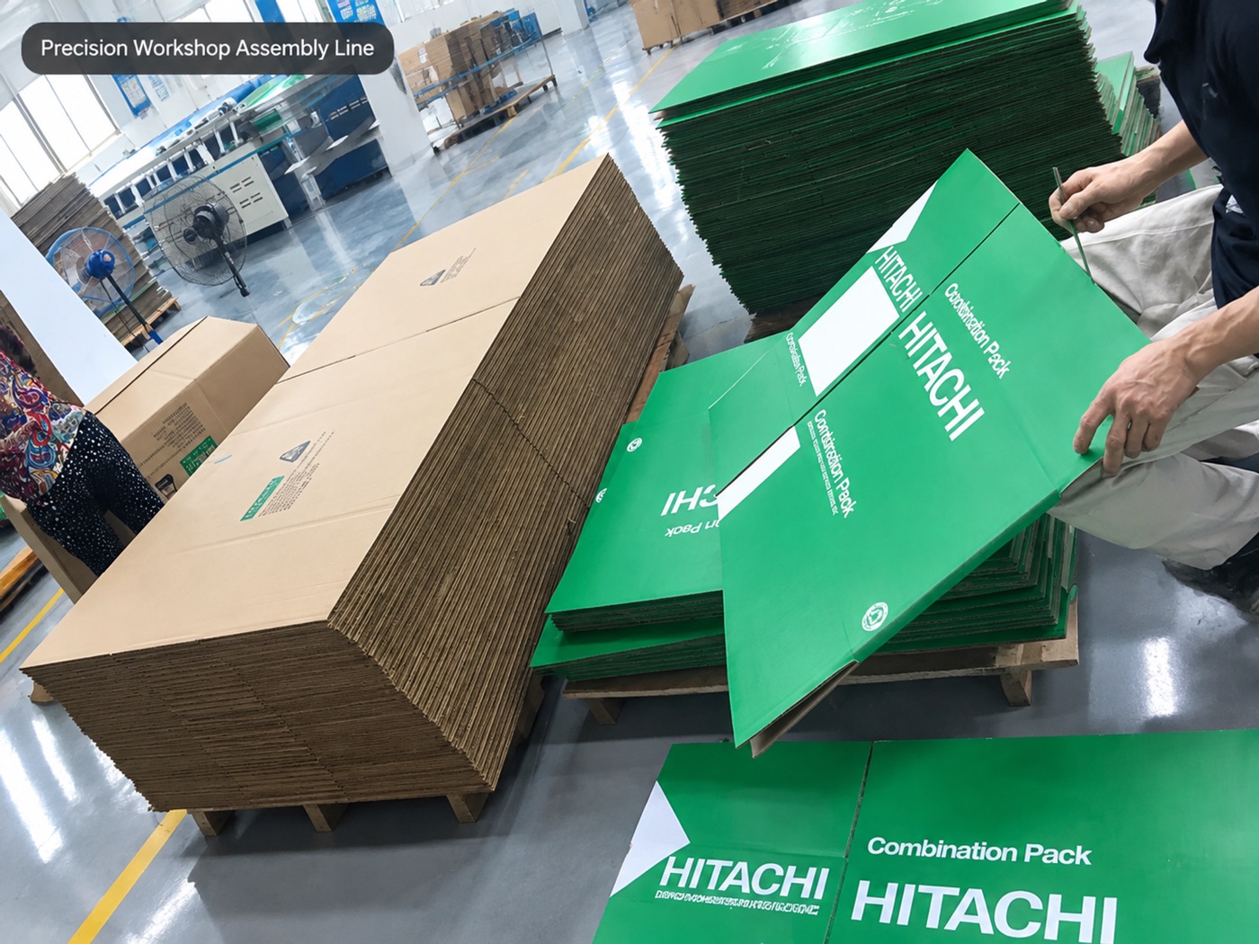 Workshop operator assembling green Hitachi printed corrugated packaging